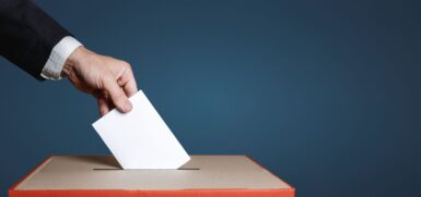 C'est une photo représentant une main en train de glisser une bulletin dans une urne de vote